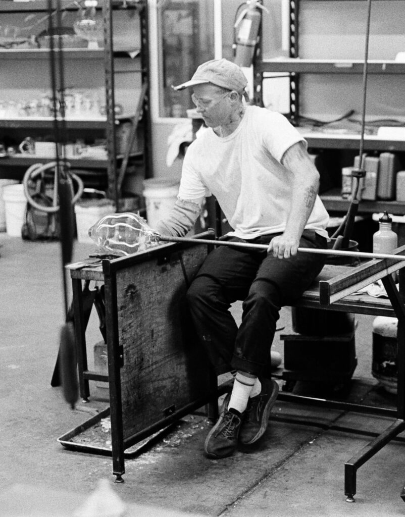 a person in a white shirt and hat blowing glass