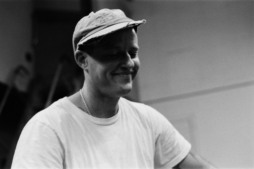 A black and white image of a white person with a hat on, smiling, eyes closed and white t-shirt