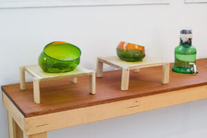 Image of two green blown glass bowls sitting next to each other, each on their own small wooden stool.