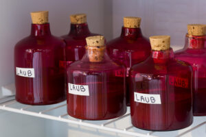 Image of a shelf inside a small fridge stacked with pink blown glass bottles with a brown liquid inside of each of the vessels. There is a label on each bottle that reads Laub.