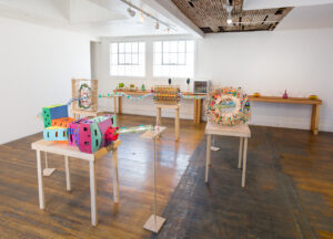 Image of a several sculptures on table tops that are a fantastical representation of the Large Hadron Collider. It is made of hamster tubes, KNex, popsicle sticks and foam. It as a playful feel with a lot of bright colors.