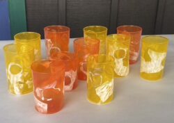 ten yellow and orange blown glass cups with a thin white layer on part of the surface of the cup