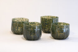 four blown glass cup with green and blue speckled color. It is round with ridges on the sides.