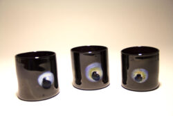 Three black blown glass cups with an iridescent indentation on the side of the cup