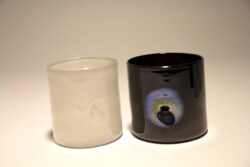 One black blown glass cups with an iridescent indentation on the side of the cup and one white blown glass cup