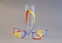 A set of four clear blown glass cups with a red, yellow and blue circle on the surface. There is also a tall pitcher with the same design.