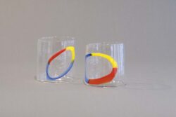 Two clear blown glass cups with a red, yellow and blue circle on the surface.
