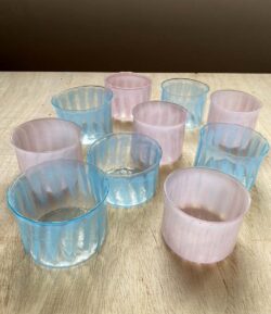 ten blown glass cups, five of them are pink and five of the are blue. they have a pattern of ridges on the surface.