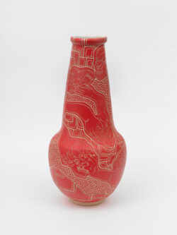 Skeletal III
2022 A red wheel thrown ceramic vessel that is wider at the bottom, has a long conical neck and a white interior. The surface has intricate carvings of hands holding a skull in various positions representing different Cranial Sacral holds.