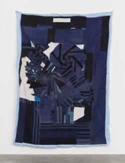 Water 2022 A predominantly indigo blue quilt, with silk white and black linen accents. There is an intense spiral in the center of the quilt that looks like a Hurricane. The quilt is framed in a soft icy blue linen. The quilt is hanging on a white wall.