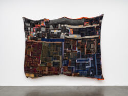 Earth 2022 A large landscape pillowy quilt. The quilt is made out of Harris tweed scraps of various color and shape. It is sewn together to look like an abstracted areal view of a landscape. The quilt is overstuffed and pinched in different places giving it a pillowy thickness. The back of the quilt is an orange satin material that can be seen from the front around the edges. It is hanging on a white wall stretched from its corners. There is a heaviness and weight to it that makes it sag.