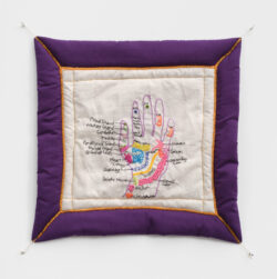 Body III 2022 A colorful embroidered diagram of a reflexology chart of the hand. It is on a quilted white background with a purple frame and gold thread accenting the outline.