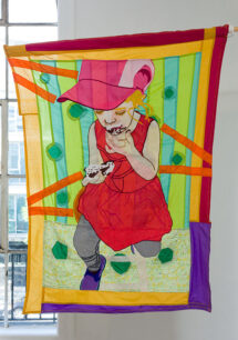 A hanging flag with different shades of green stripes as a background. On the foreground there is a young white child with a pink hat and pink dress eating an ice cream sandwich. the flag is framed in red, purple and orange. The light from the window shines through it, illuminating the colors.