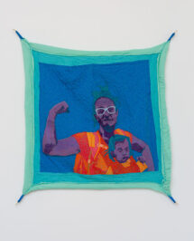 A quilted tapestry of a mom flexing her bicep and holding her child on her chest. The baby seems to flexing her arm as well. They are purple with blue hair, wearing orange clothes. The background is dark blue and the border of the quilt is a sea green. It is stretched on the wall from all four corners.