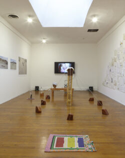 Installation view
foreground:
Entrance Mat
2014 Installation view of the exhibition Oh Be Gentle. In the foreground there is a beaded mat on the floor. The room is filled with various wood and glass objects and vessels. There are photographs on one wall and drawings on the other wall. The far wall has a tv screen that is playing a video.