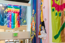 Image of a stairwell with colorful banners hanging from the wall telling the life story through sewn pictures, much like a comic book, of the dog Mr. Snuggles.