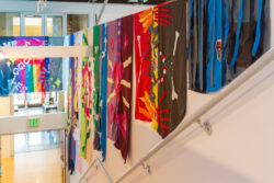Image of a stairwell with colorful banners hanging from the wall telling the life story through sewn pictures, much like a comic book, of the dog Mr. Snuggles.