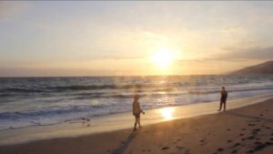 A video still of two people walking towards each other on the beach